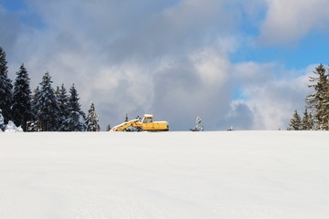 Gelber Bagger in verschneiter Winterlandschaft, Allgäu