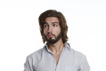 Handsome guy with stylish haircut and fuzzy beard looking sideways having suspicious skeptical expression. Bearded young man in grey shirt expressing suspicion, doubt or distrust posing in studio