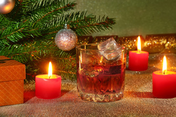 christmas decoration with glass of whiskey or cognac, christmas candles, tree and gift box on a sparkling background. New Year decoration.