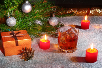 christmas decoration with glass of whiskey or cognac, christmas candles, tree and gift box on a sparkling background. New Year decoration.