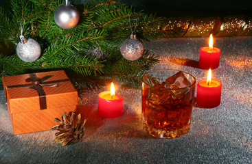 christmas decoration with glass of whiskey or cognac, christmas candles, tree and gift box on a sparkling background. New Year decoration.