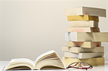 Open book, glasses and pile of books on the white table