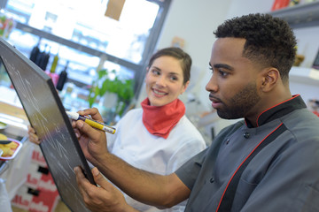 chef writing specials on chalkboard in delicatessen