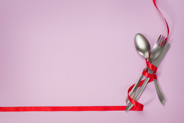 Cutlery with red ribbon as border on pink background with copy space