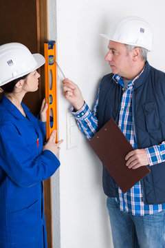 female apprentice checking level of door frame while architect supervises