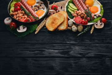 Full English breakfast with fried eggs, sausages, beans, toasts and coffee on copy space background. On a black wooden background.