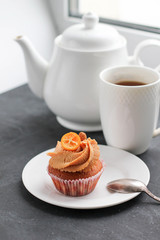 A teapot, a cup of tea and a caramel cupcake.