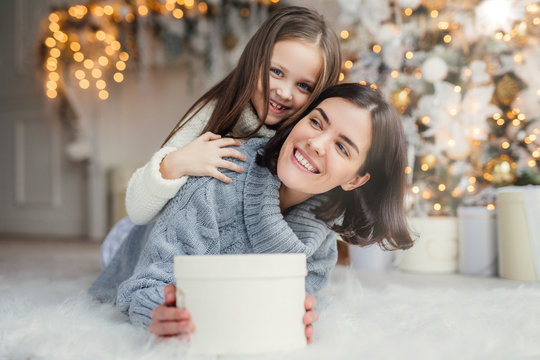 Happy female model with short dark hair and her adorabe small girl have fun together, celebrate Christmas, exchange presents, have smiling expressions, have joy. Friendly family with presents