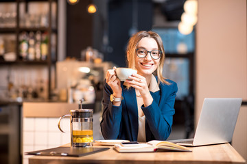Young businesswoman strictly dressed in the suit drinking tea during the break at the modern cafe interior