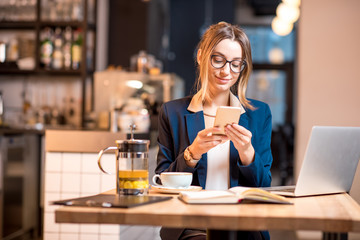 Young businesswoman strictly dressed in the suit talking phone while working with laptop at the modern cafe interior