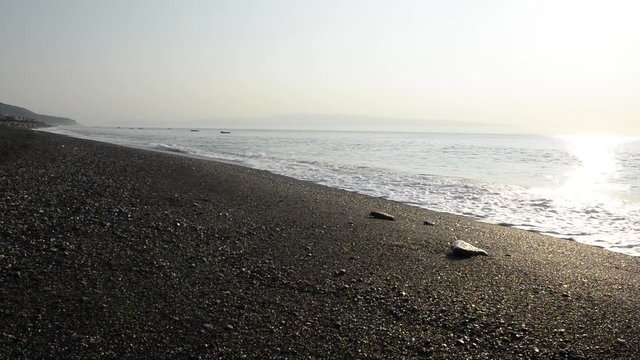 Onde del mare investono sassi sulla spiaggia nelle prime lucu della giornata una estiva