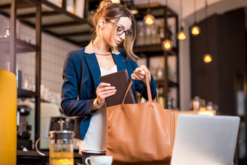 Young businesswoman packing stuff into the bag during the coffee break in the modern cafe