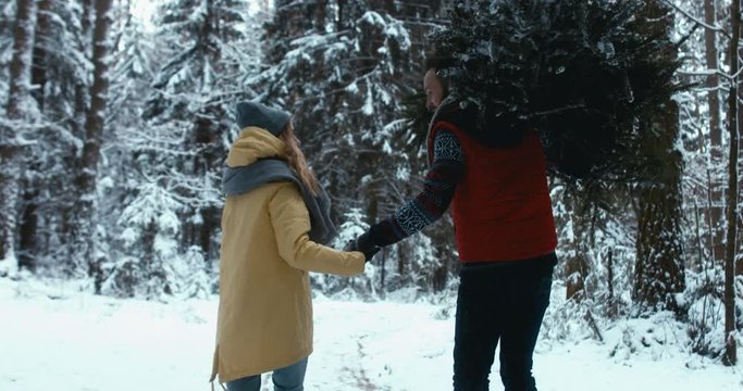 TRACKING Beautiful Caucasian couple or family bringing a Christmas tree back home from forest. Holidays, lifestyle. 4K UHD 60 FPS SLO MO