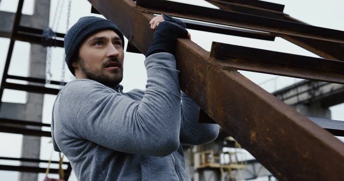 Sporty caucasian man doing pull ups in the old plant ruins on the cold grey day in the moning. Close up. Portrait shot