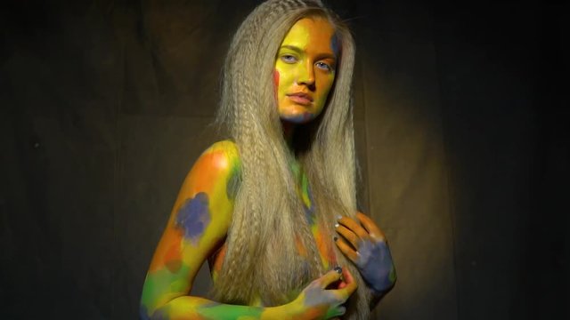 Slow motion shooting of a long-haired naked woman in abstract body art that poses on the camera