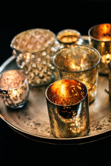Sparkling candle cups with tealight candles burning golden on a tray