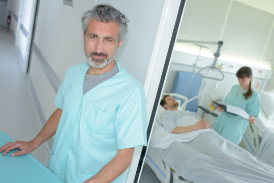 Portrait Of Confident Male Nurse With Colleagues Examining Patient