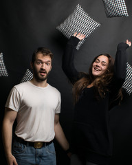 cheerful young people throwing pillows on a black background. young cheerful couple. smiling girl and surprised guy
