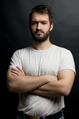 Young attractive sporty man with a beard on a black background. serious, stern look of a man