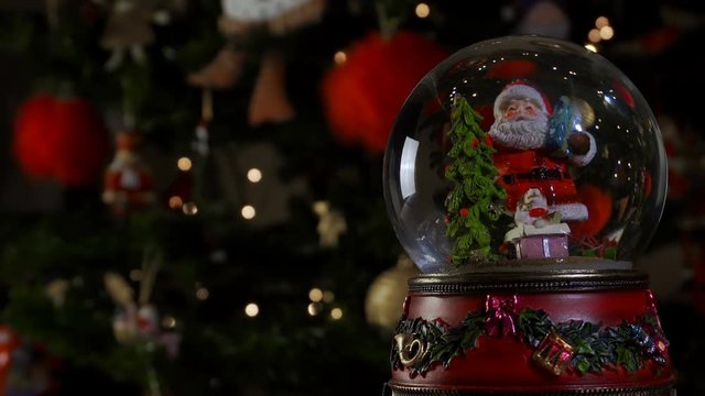 Christmas snow globe ball before blurred background with space for text. 
Decorating Christmas dome ball with Santa Claus before a lit Christmas tree.