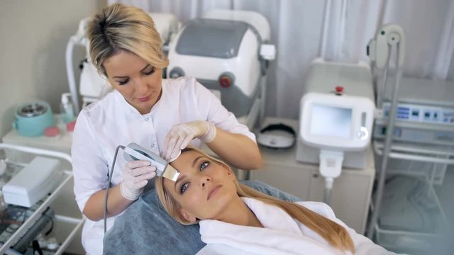The cosmetologist makes the procedure ultrasonic face peeling of the facial skin of a beautiful, young woman in a beauty salon