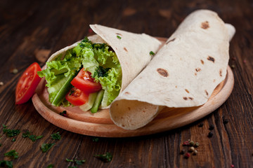 Fototapeta na wymiar burrito with greens, cucumbers, tomatoes and sausages on a round wooden board on a wooden background