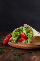  burrito with greens, cucumbers, tomatoes and sausages on a round wooden board on a wooden background