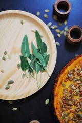 Golden pumpkin pie, sprinkled with seeds on a black table next to a wooden Board sage leaves, top view closeup