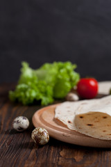 cooking burrito with greens, cucumbers, tomatoes and sausages on a round wooden board on a wooden background