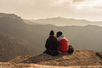 Couple sitting on high mountain peak watching the beautiful and surreal wilderness landscape in front of you in Siurana