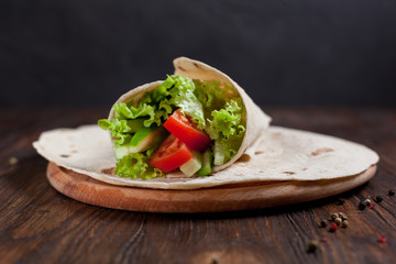  burrito with greens, cucumbers, tomatoes and sausages on a round wooden board on a wooden background