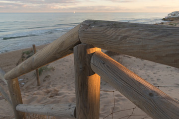 Wooden staircase and railing access to the beach sand at sunset with somewhat cloudy sky an sea with waves in Guardamar, Spain