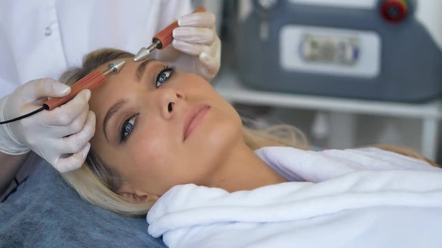 Close-up of beautiful woman receiving facial microcurrent treatment from therapist at beaty salon