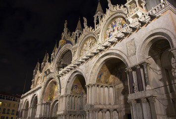 Fototapeta na wymiar Facade view of Saint Mark's Basilica (San Marco) at night in Venice / Italy. Iconic cathedral with a cavernous gilded interior, myriad mosaics & an on-site museum.