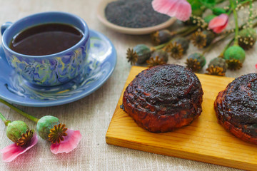 Sweet bun with flax seed and poppy and cup of tea on table.