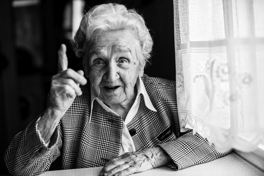 Elderly lady speaks sitting at the table. Black and white portrait.