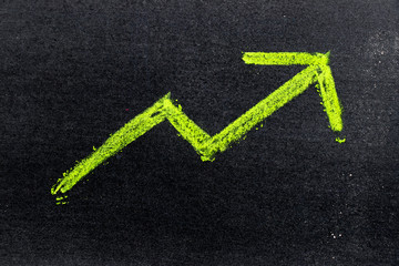 Green color hand drawing chalk in arrow up shape on black board background (Concept of revenue increase, stock or business growth)