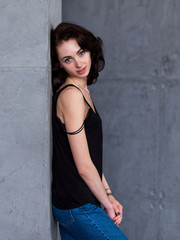Pretty young Caucasian model with blue eyes and brown hair standing in casual clothes at wall indoors smiling looking at camera