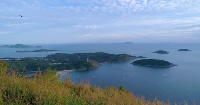 Aerial: Beautiful view with a bird in the frame from the edge of the mountain overlooking the sea, beach, wind mill, islands and a lot of ships in the bay. Phuket. Thailand.