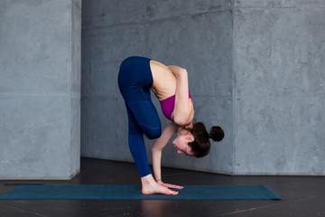 Flexible young woman performing one-leg balance exercise doing half bound lotus standing forward...