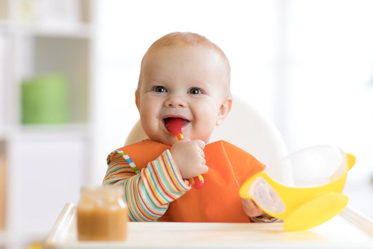 Happy infant baby boy spoon eats itself