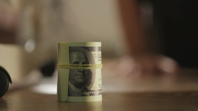 Closeup of the hand of a man finds and pulls out from under the bed a pack of dollar bills
