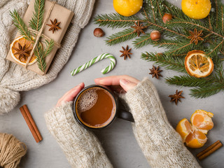 Winter hot drink female hands in a sweater holding a Cup of hot chocolate on a gray concrete background tangerines scenery