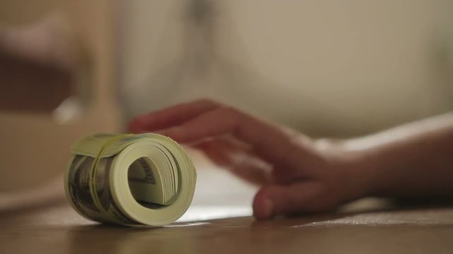 Close-up of a woman's hand finds and pulls out from under the bed a pack of dollar bills