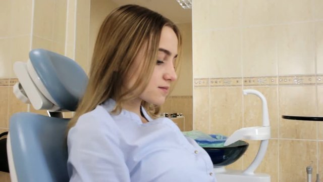 The girl sitting in the dentist's chair uses a smart phone