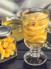 Tea with ginger and lemon in a glass cup and yellow sweets on a wooden background