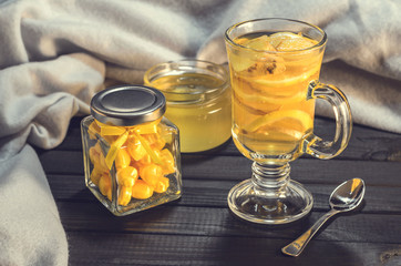 Tea with ginger and lemon in a glass cup and yellow sweets on a wooden background