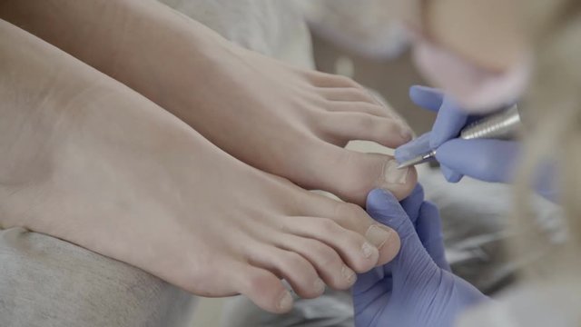Close-up of pedicurist uses apparatus at client's feet. Sharp tip of wizard carefully spends over skin during provision of nail care services.