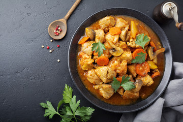 Goulash traditional Hungarian dish. Stew with pepper and tomato sauce in ceramic plate on dark black stone or concrete background. Selective focus. Top view.