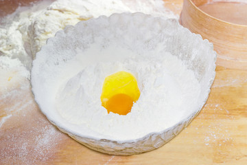 Bowl with flour and broken egg on the table